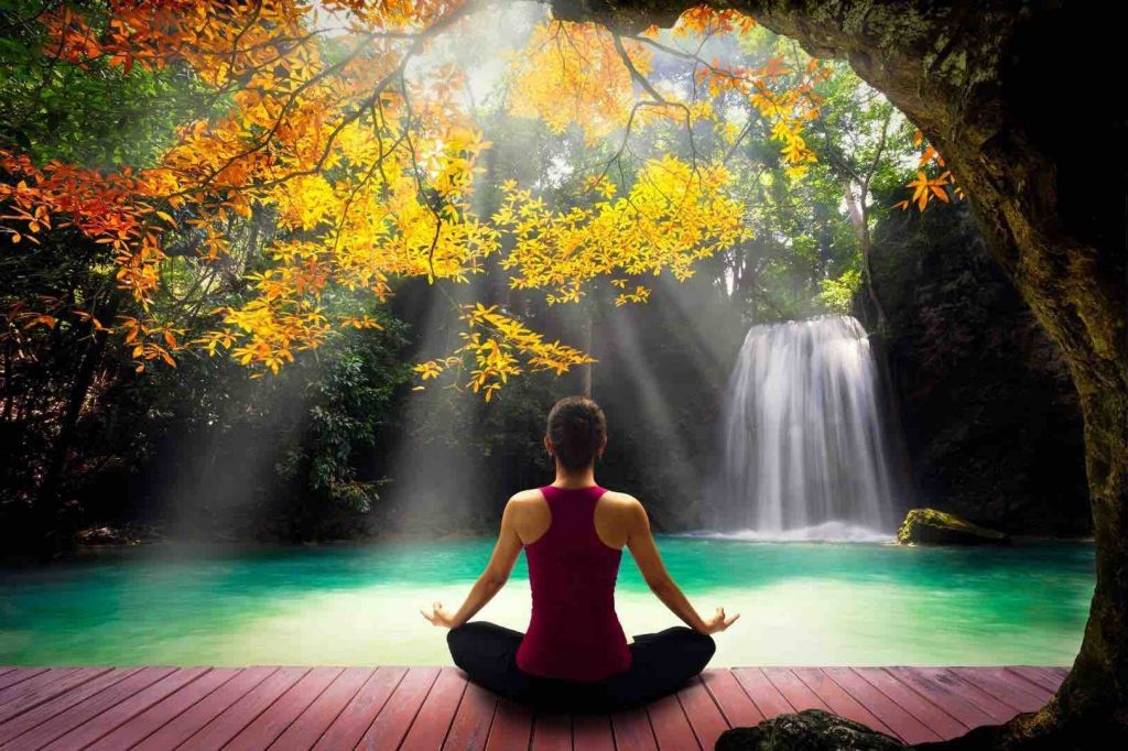 Woman Meditating in Colourful Forrest by a Lake and Waterfall