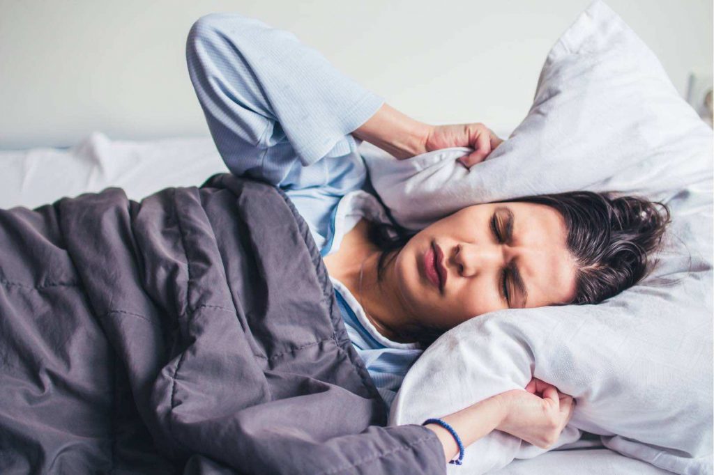 Woman with Insomnia Can't Sleep Holding Pillow Over Her Ears