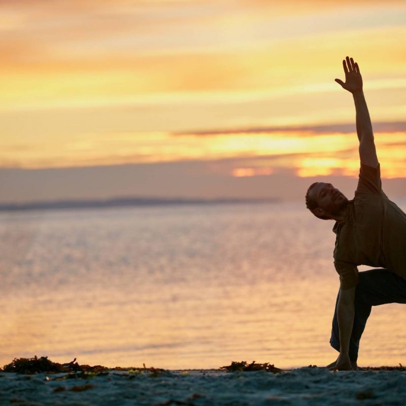 Man Doing Warrior Yoga Pose with Sunset and Ocean in the Background