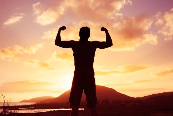 Powerful Man Standing Flexing Muscles with View of Mountain with Sunset