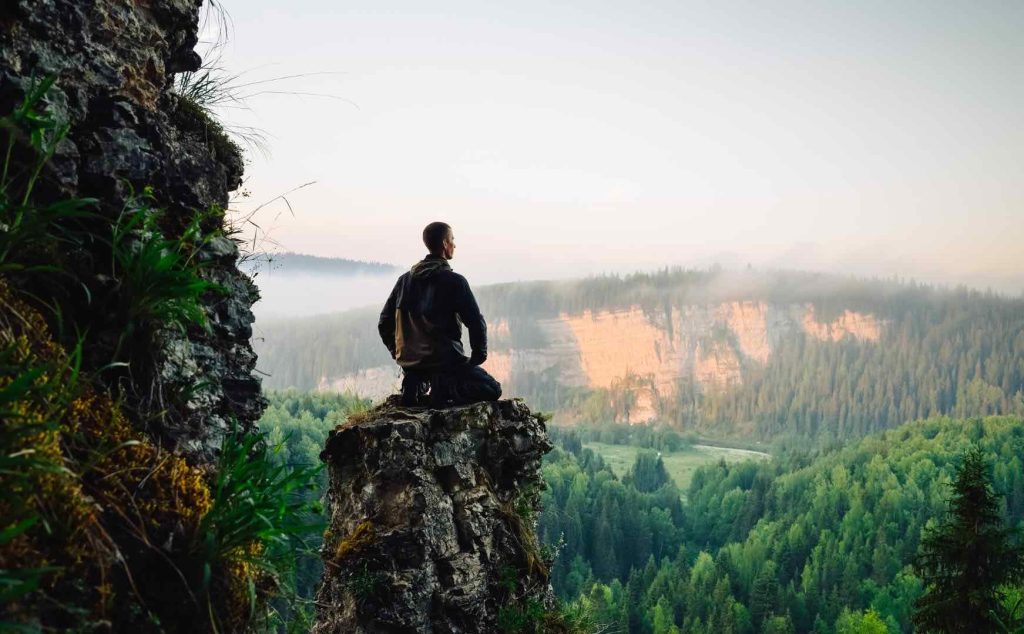 Man Meditating on Rock with Beautiful View of Forest and Hill