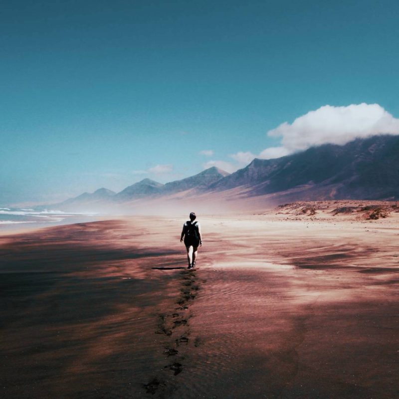 Man Walking on Beaching Taking a Journey Through Life with Blue Sky View and Mountains