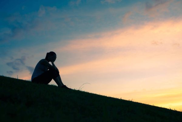 Silhouette of Woman Sitting on a Hill Depressed with Hands on Head Upset and Sad with Sunset Behind