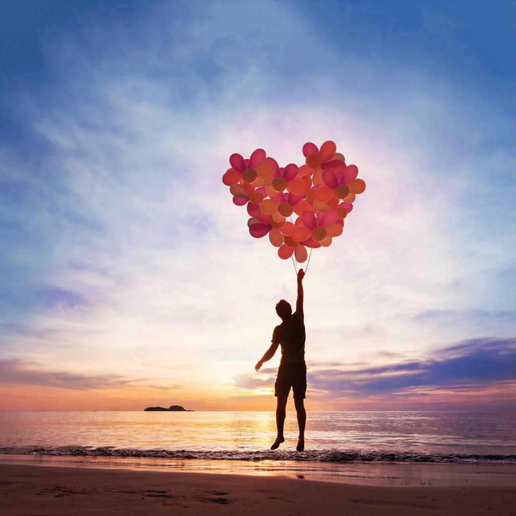 Man Holding Balloons in Shape of Heart Going Up Into the Sky