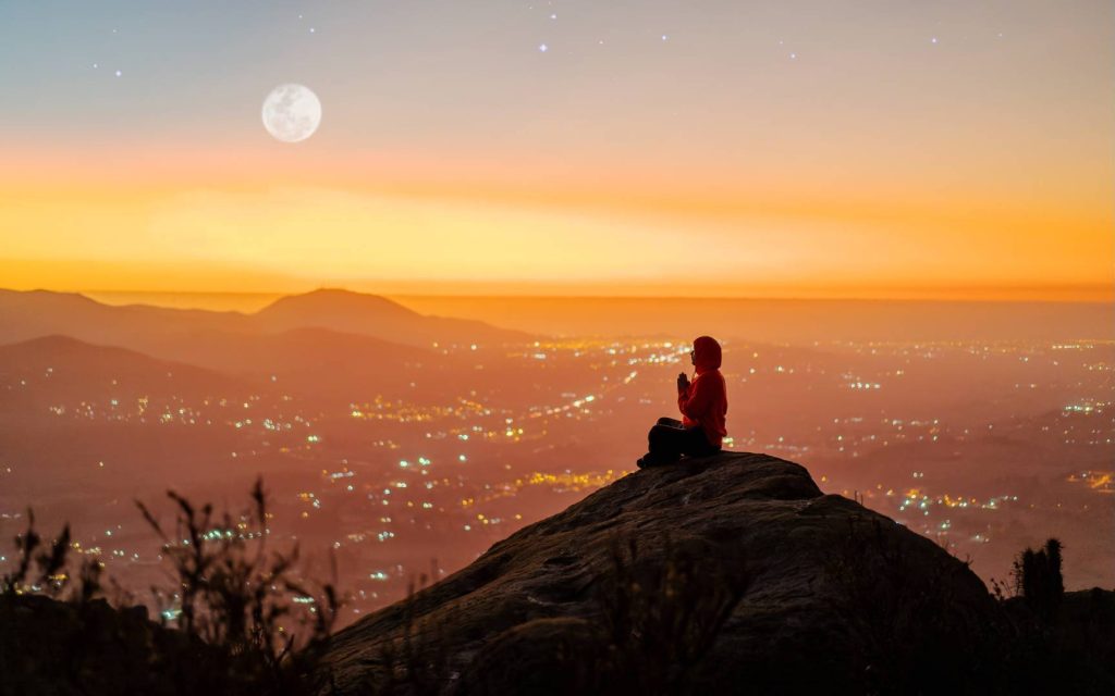 Man Meditating on Hill with View of City at Sunset