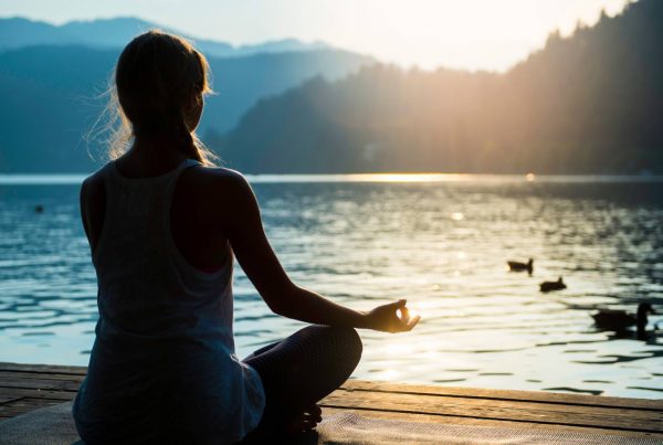 Woman meditating by Lake with Views of Hills and Trees