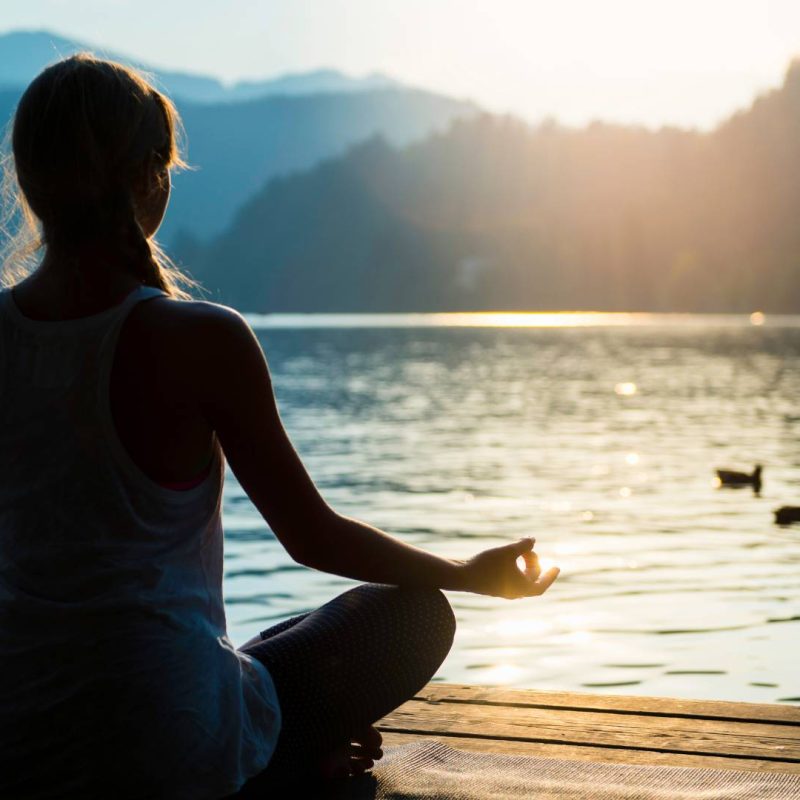 Woman meditating by Lake with Views of Hills and Trees