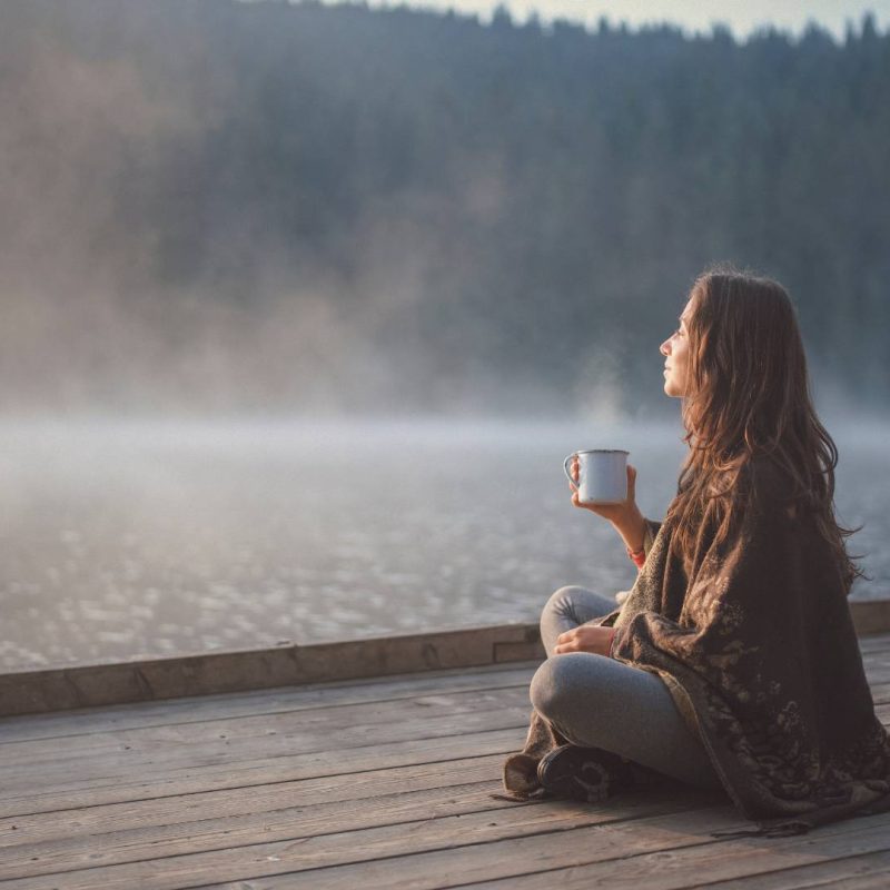 Woman Sitting with Hot Cup of Tea with View of Lake