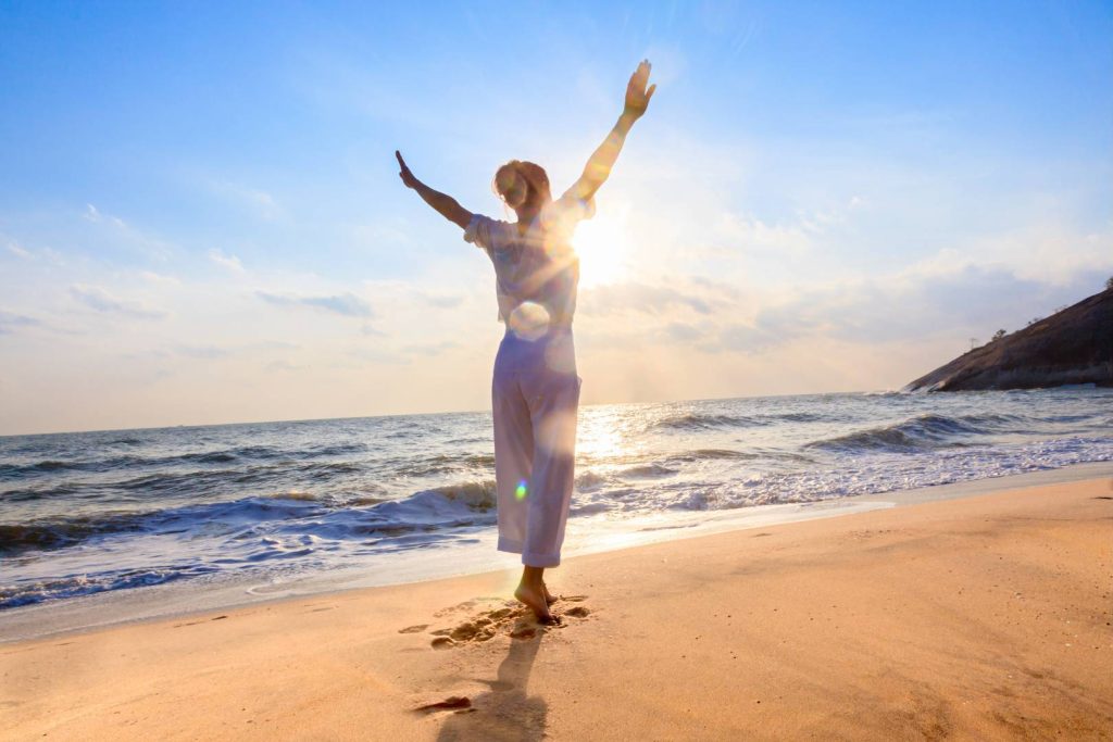 Happy Woman with Arms Up Wide Open on Beach in Sun