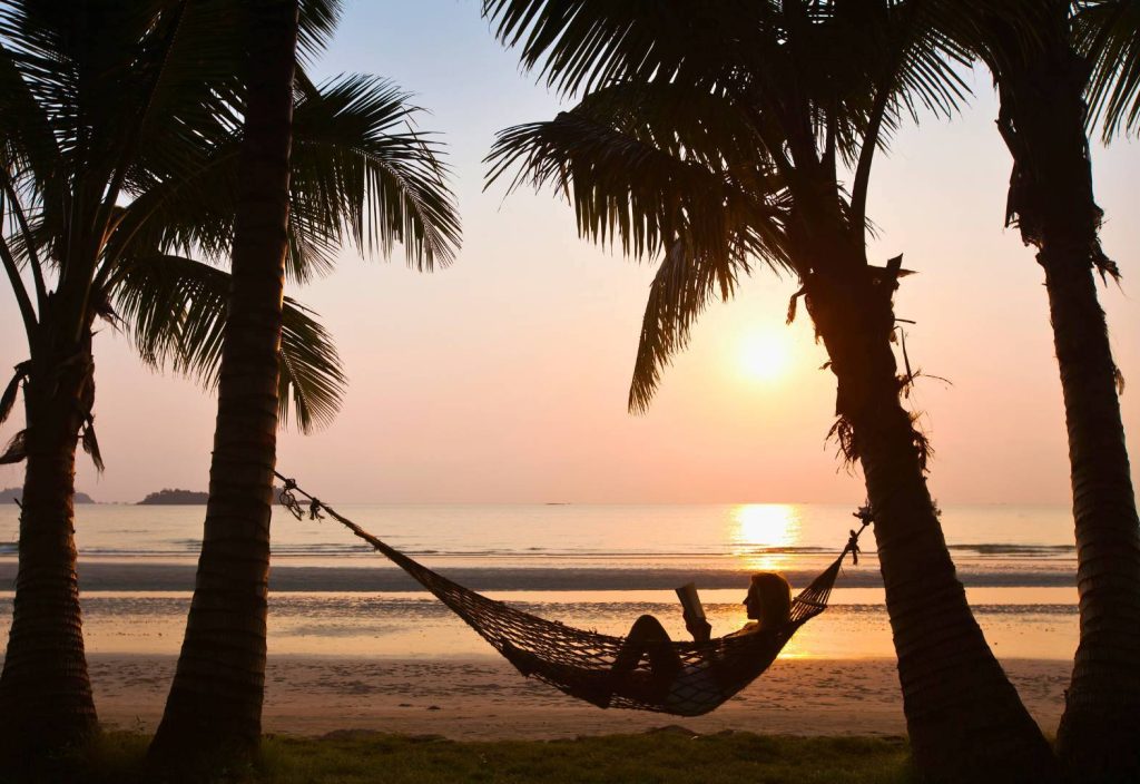 Woman Relaxing Reading on Hammock with Palm Trees and Sunset