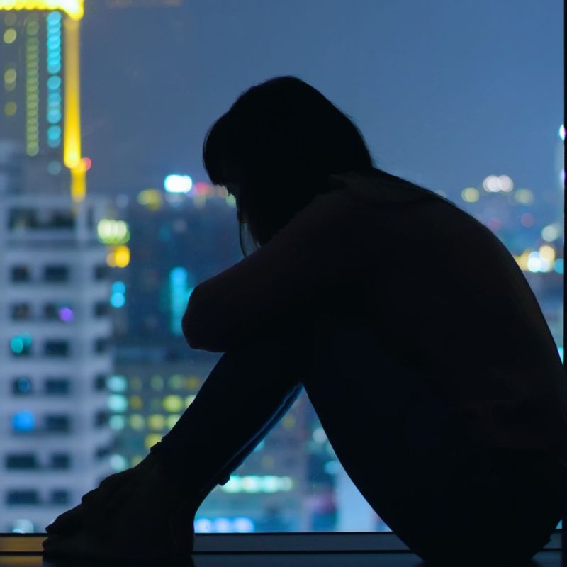 Woman Sitting on Windowsill Depressed and Sad with City View