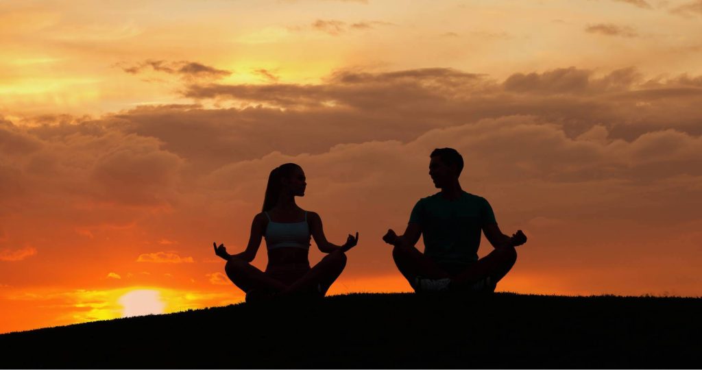 Woman and Man Silhouettes Meditating together During Sunset