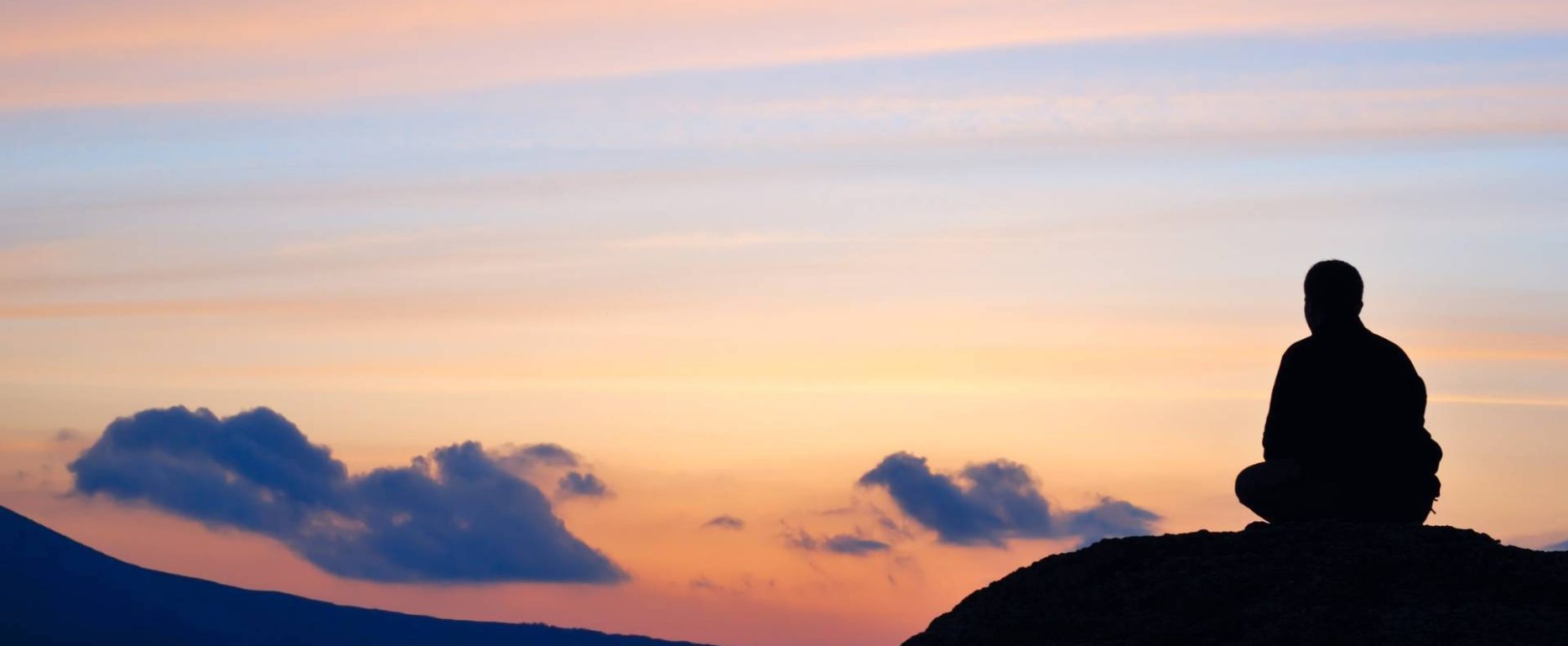 Silhouette of a Man Meditating on a Hill with Sunset Background