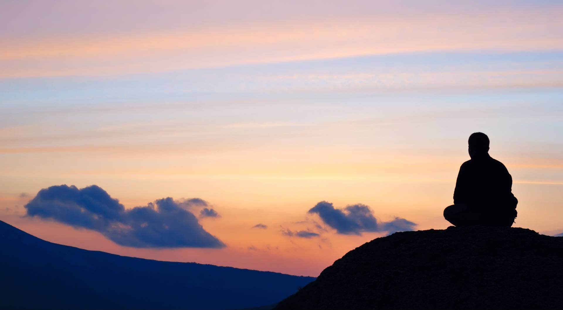 Silhouette of a Man Meditating on a Hill with Sunset Background