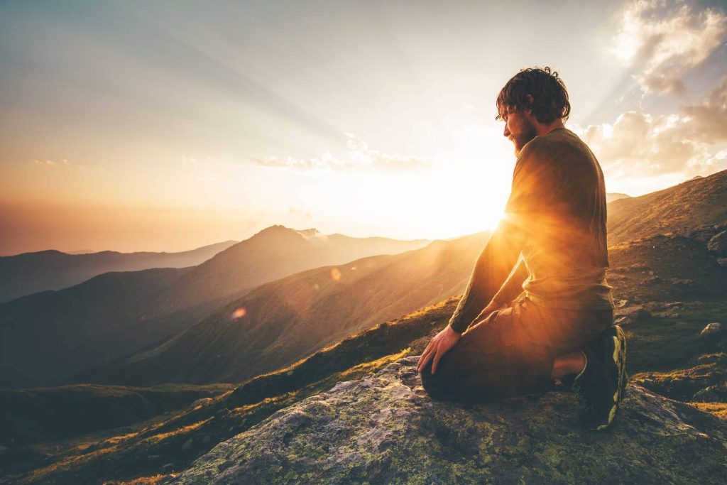 Man Meditating on a Mountain with Sunset in the Background