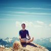 Man Meditating on Cliff with Blue Sky and Clouds in Background