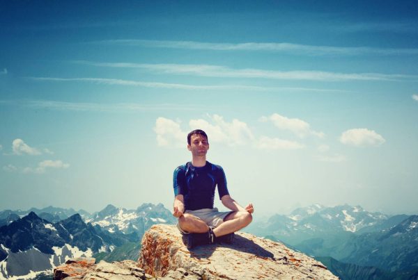 Man Meditating on Cliff with Blue Sky and Clouds in Background